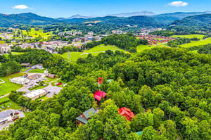 Aerial view showcasing the property nestled among lush greenery and rolling hills, with vibrant mountain scenery and a charming nearby town in the distance.