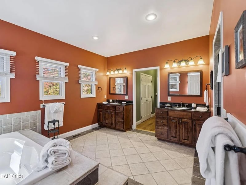 Step into your spacious bathroom retreat with warm terracotta walls, dual vanities with elegant lighting, and plush towels waiting for you. Sunlight streams through the windows as you prepare for the