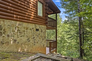 Rustic log cabin nestled in lush forest with stone foundation and private balconies overlooking treetops. A peaceful wooded retreat perfect for nature lovers.