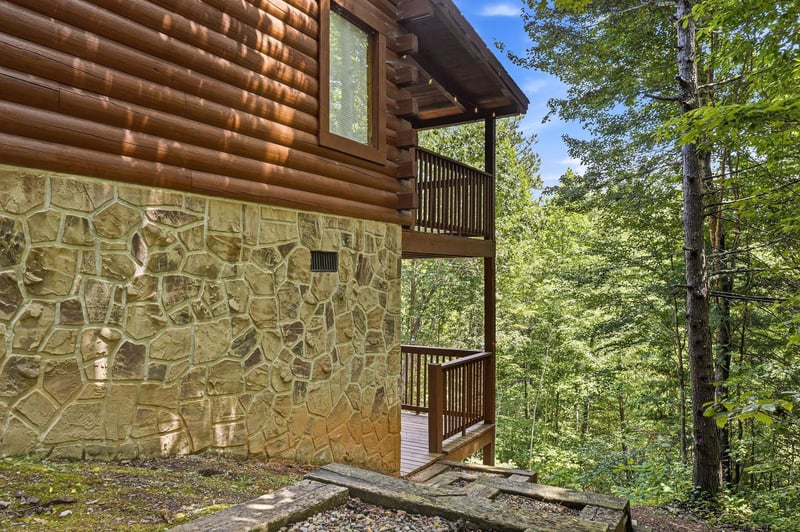 Rustic log cabin nestled in lush forest with stone foundation and private balconies overlooking treetops. A peaceful wooded retreat perfect for nature lovers.