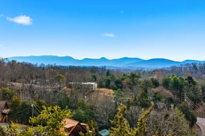 Stunning mountain vistas stretch across rolling blue ridges, framed by mature trees and peaceful residential surroundings in this scenic area.