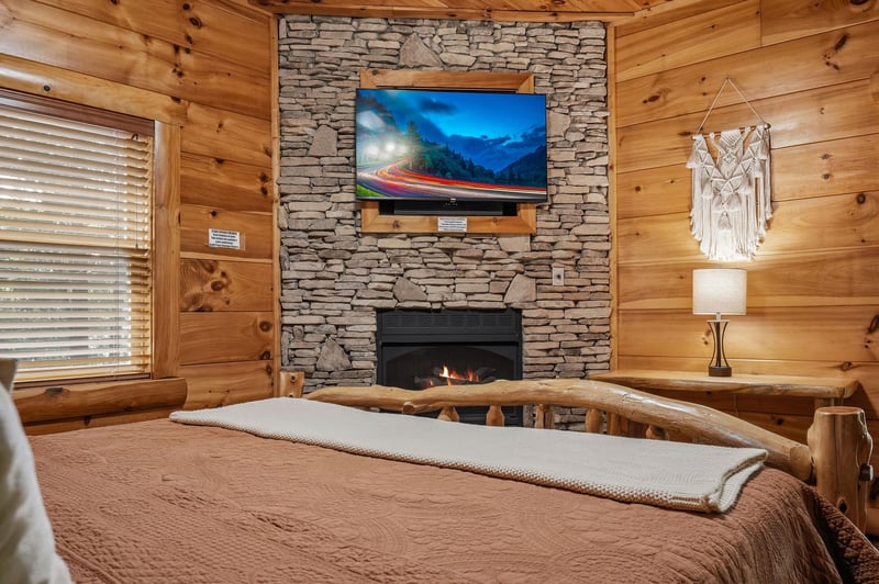 Settle into your cozy cabin bedroom where rustic wooden walls and a crackling stone fireplace create a warm mountain retreat. The handcrafted log bed invites restful nights in this peaceful space.
