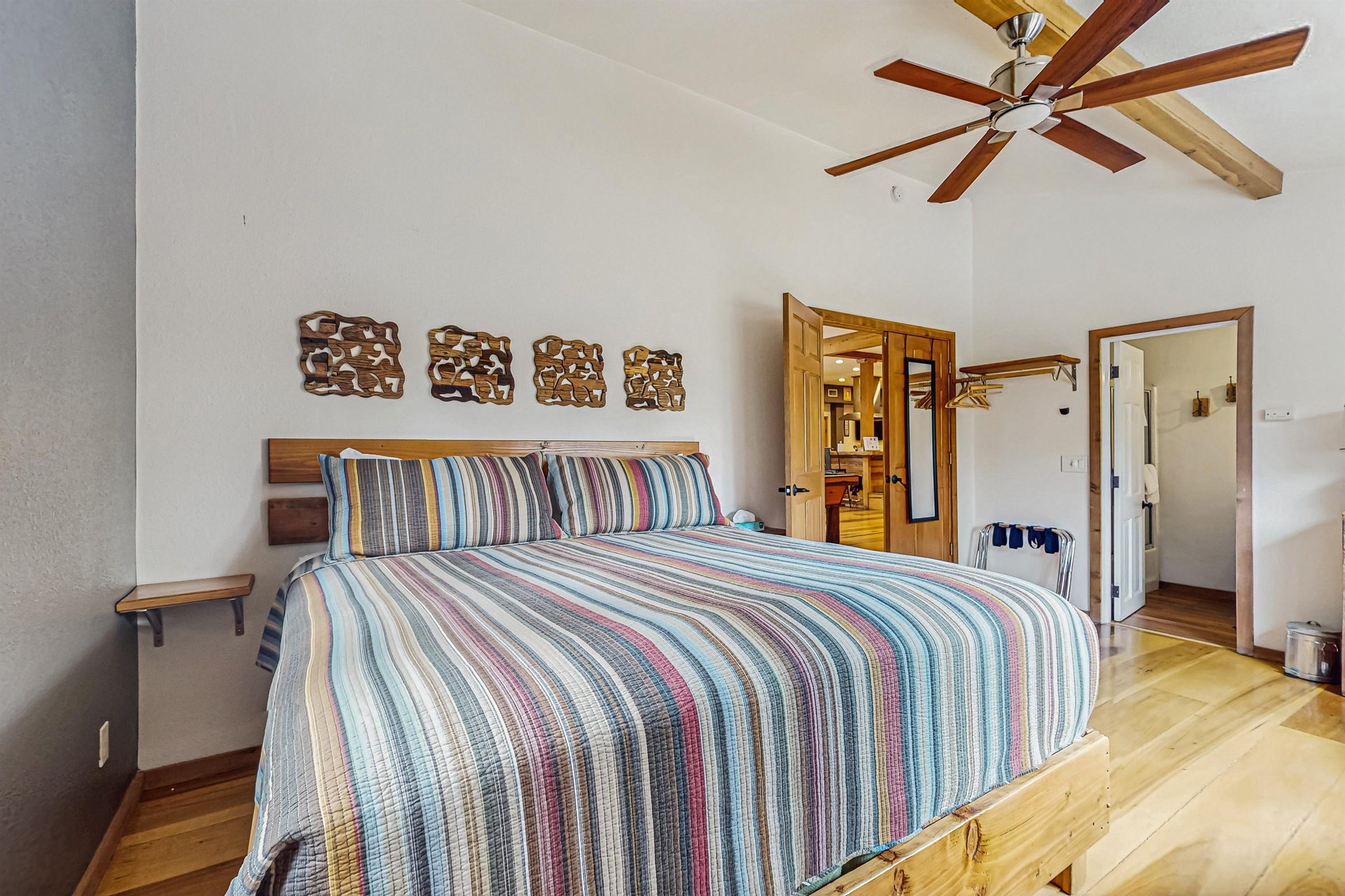 Another view of the primary bedroom, showing direct access to the private en suite bathroom, plus a handy wallmounted clothing and luggage rack near the doorway — along with the ceiling fan and smart TV for added comfort.