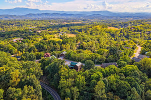 Aerial view of the property nestled among rolling hills and lush forests, with the majestic Blue Ridge Mountains framing the horizon. Scenic mountain surroundings define the tranquil location.