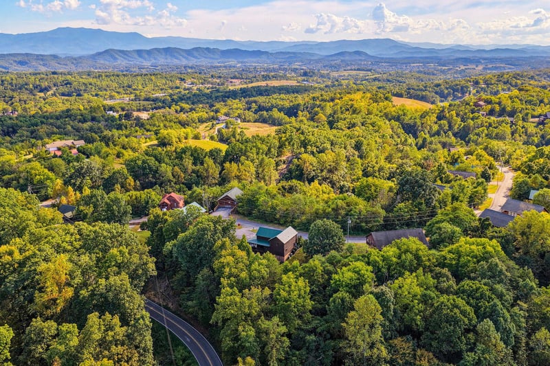 Aerial view of the property nestled among rolling hills and lush forests, with the majestic Blue Ridge Mountains framing the horizon. Scenic mountain surroundings define the tranquil location.