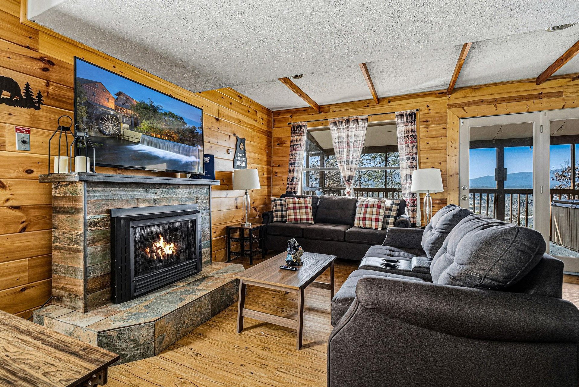 Cozy up by your crackling fireplace while enjoying mountain views from this warm cabin living room with plush seating and rustic charm.