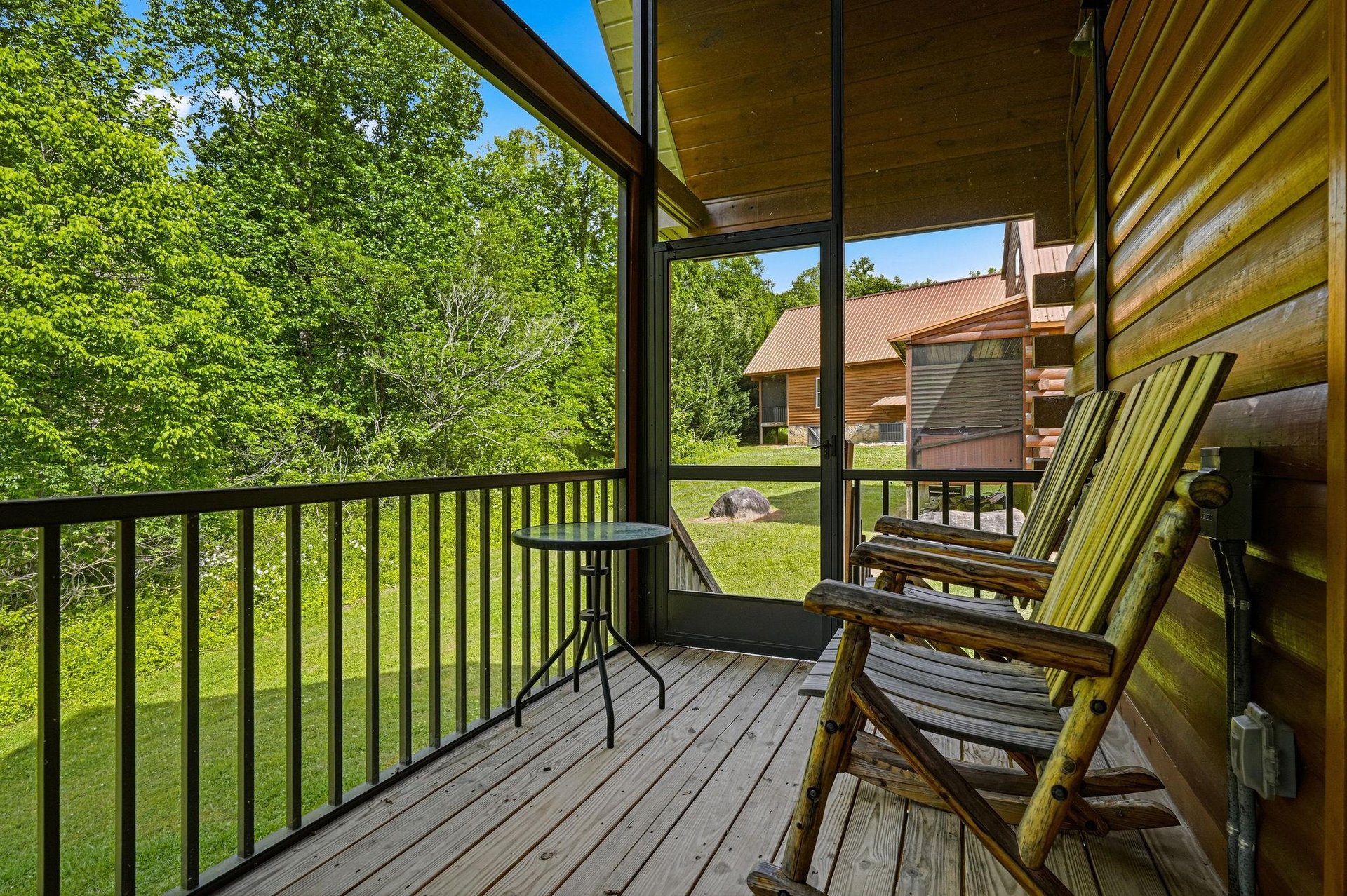 A private covered balcony with lush forest views and rustic seating invites you to unwind, sip your morning coffee, and breathe in the fresh country air.