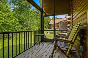 A private covered balcony with lush forest views and rustic seating invites you to unwind, sip your morning coffee, and breathe in the fresh country air.