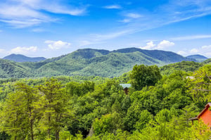 The property overlooks lush forested mountains rising against a bright blue sky.
