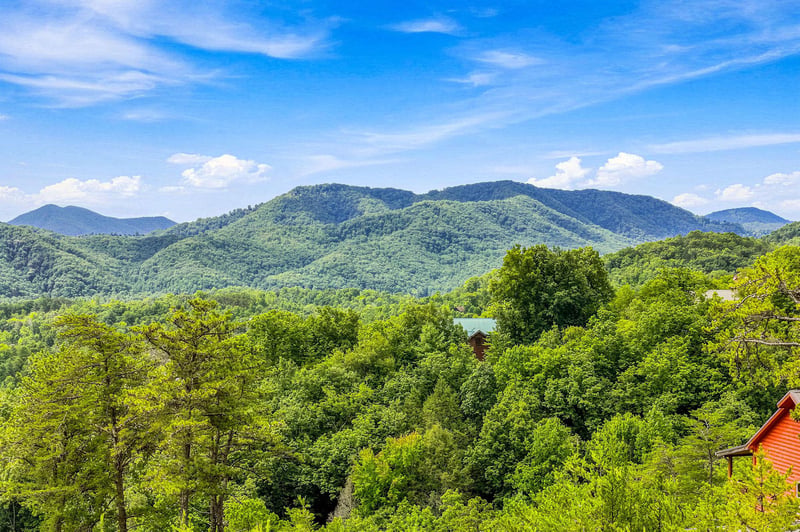 The property overlooks lush forested mountains rising against a bright blue sky.