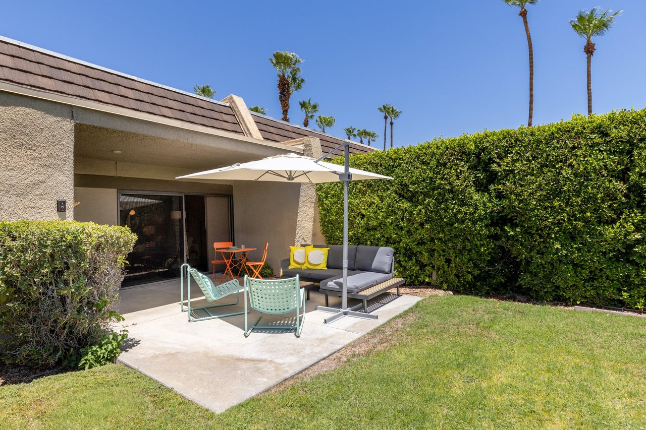 Back patio located off of the living room and primary bedroom featuring a table and chairs for morning coffee, umbrella, and ample outdoor seating.