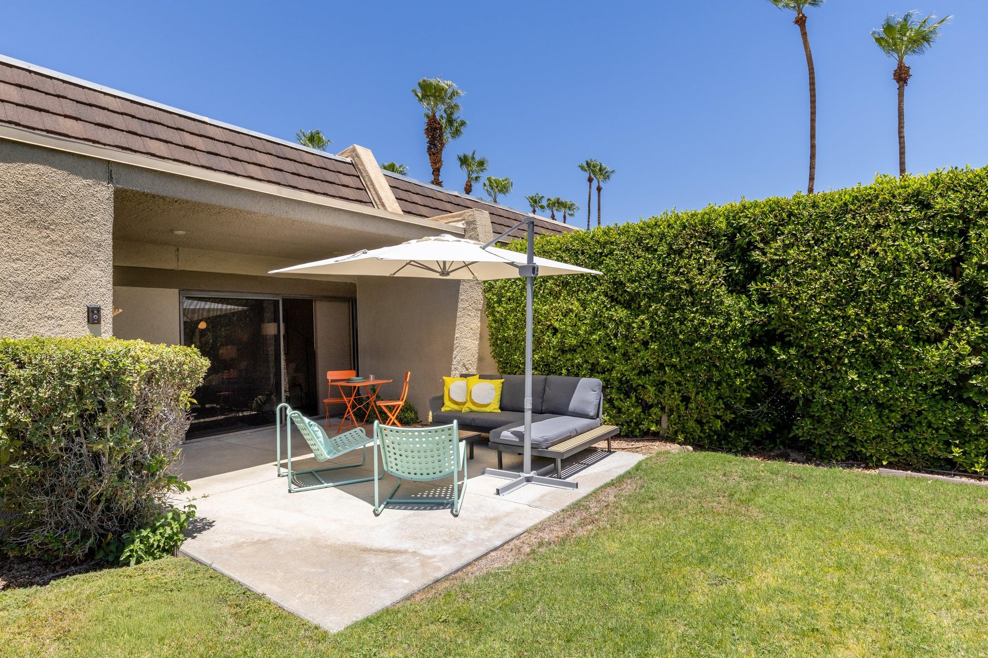 Back patio located off of the living room and primary bedroom featuring a table and chairs for morning coffee, umbrella, and ample outdoor seating.