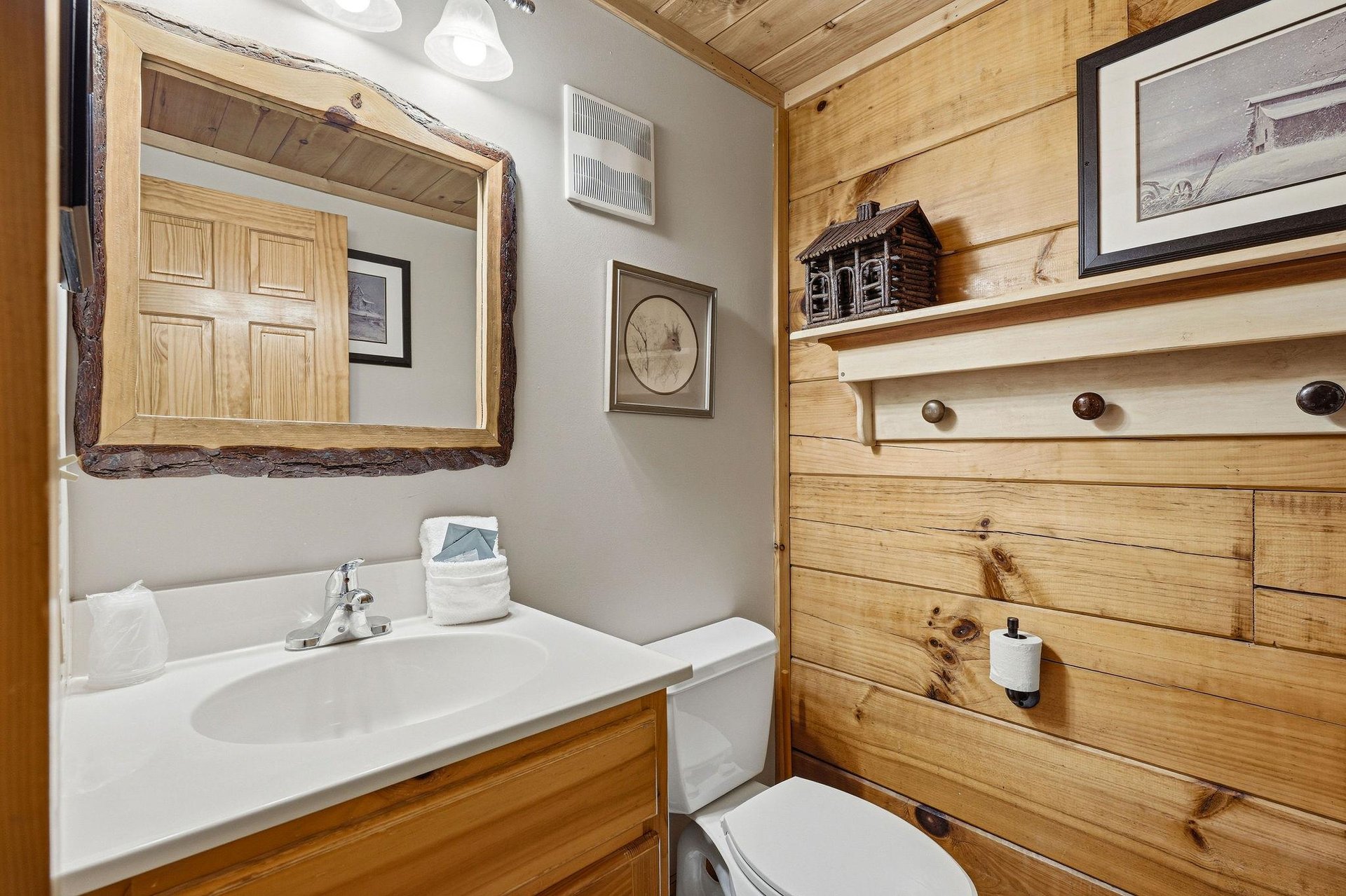 This cozy bathroom blends rustic wood with modern comfort. Enjoy the natural charm of reclaimed timber walls, a stylish vanity, and thoughtful touches like the cabin décor above.