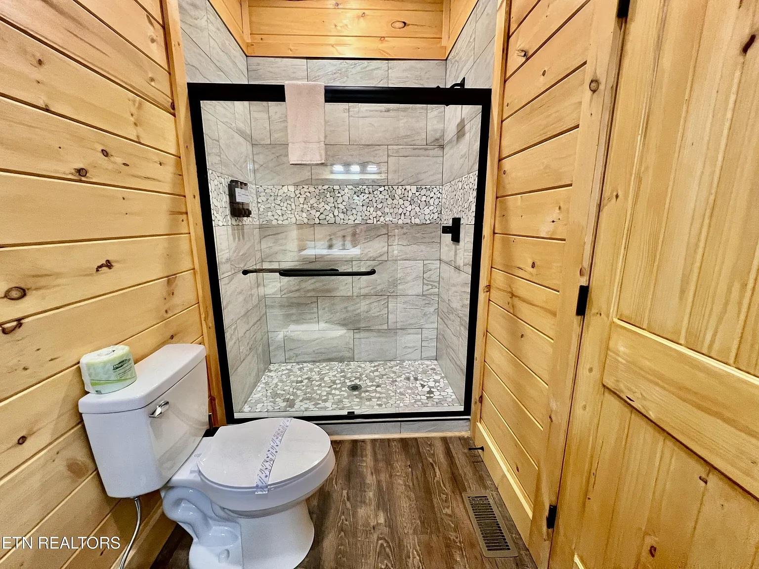 Step into your beautifully appointed bathroom featuring rustic wood paneling and a stunning tiled shower with pebble accents.