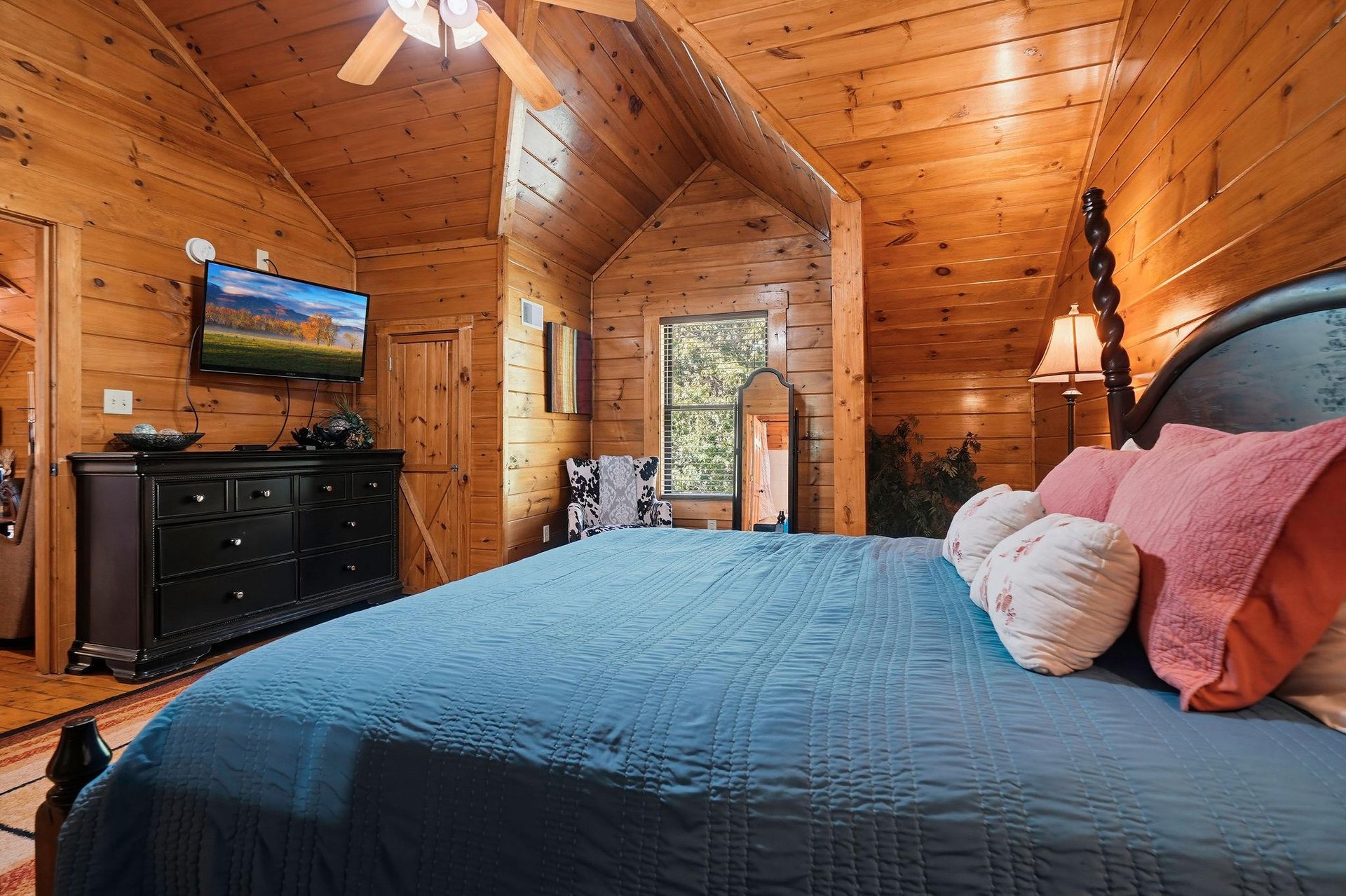 Unwind in your cozy cabin bedroom where warm wood walls meet comfortable bedding. The vaulted ceiling adds character while your favorite shows await on the mounted TV.