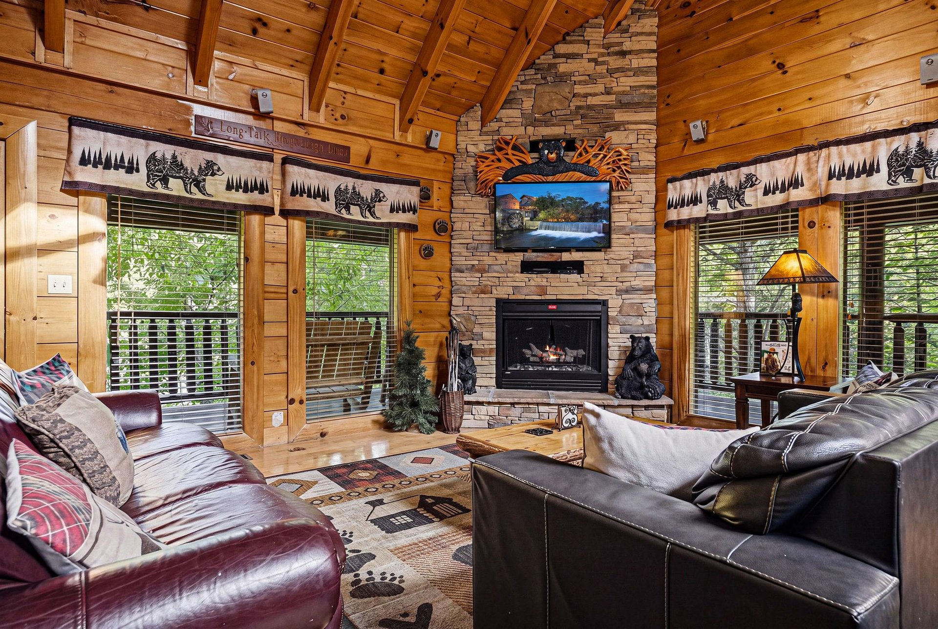 Unwind in your rustic living room with leather sofas, stone fireplace, and forest views through every window.