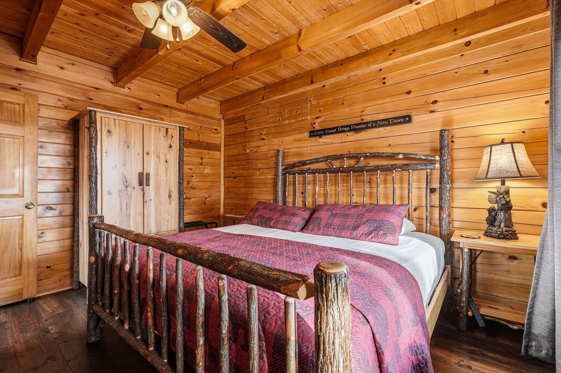 Retreat to your cozy log bedroom with rustic charm and rich red linens that promise peaceful mountain nights.