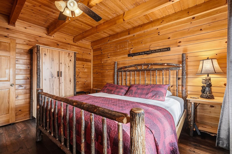 Retreat to your cozy log bedroom with rustic charm and rich red linens that promise peaceful mountain nights.