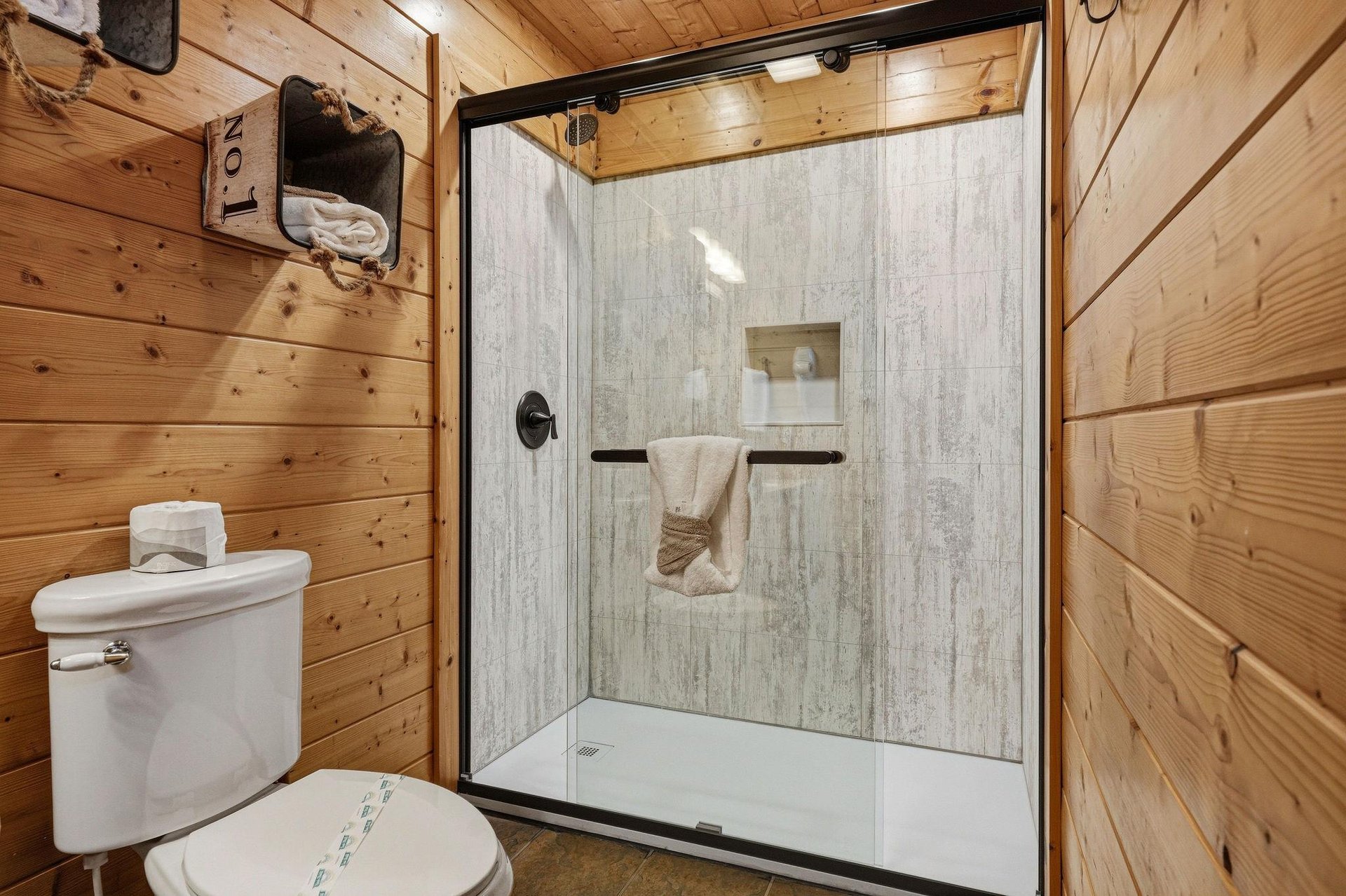 Step into your private sanctuary with this rusticchic bathroom featuring a modern walkin shower and warm woodpaneled walls that bring cabin charm to your daily routine.