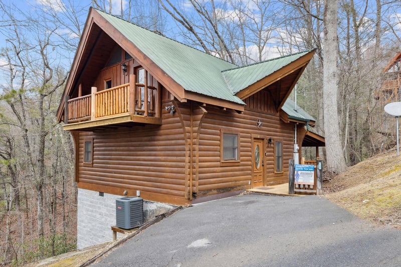 Charming log cabin nestled among tall trees with convenient paved parking and welcoming entrance.