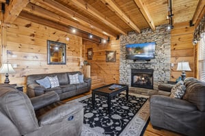 Cozy up in this rustic living room with soaring beams, stone fireplace, and plush seating for perfect mountain getaway evenings.