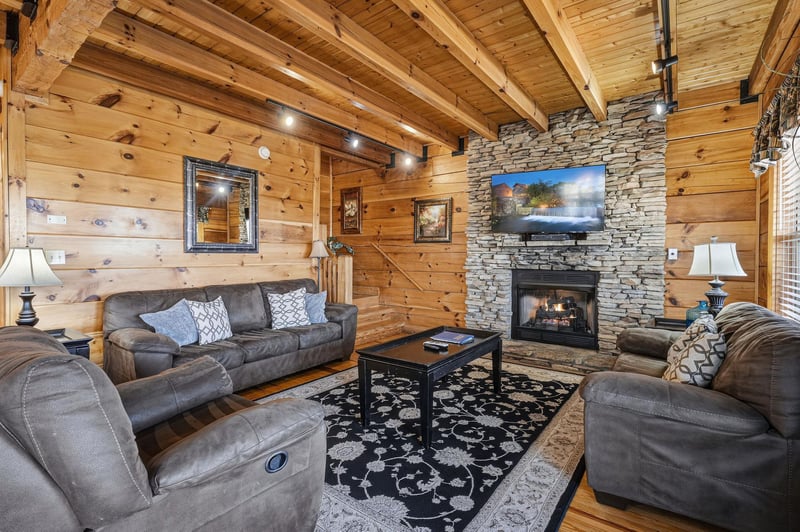 Cozy up in this rustic living room with soaring beams, stone fireplace, and plush seating for perfect mountain getaway evenings.
