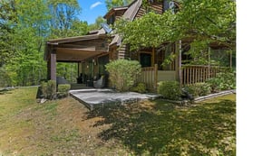 A charming wooden cabin nestled among lush trees, featuring a welcoming covered porch and peaceful forest surroundings.