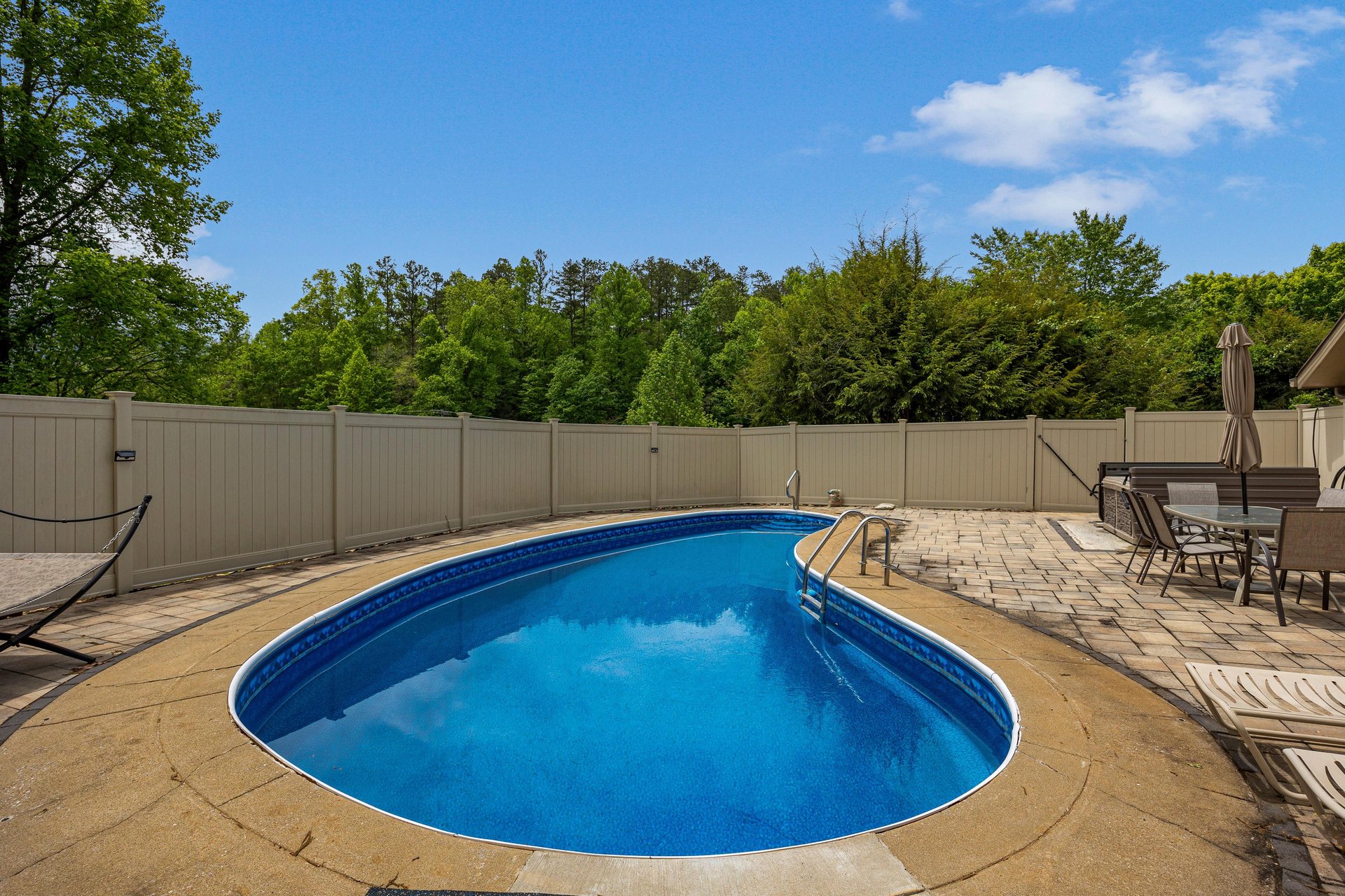 A private oasis awaits with a sparkling pool surrounded by a spacious paver deck, perfect for soaking up the sun or dining al fresco under the shade of lush greenery.