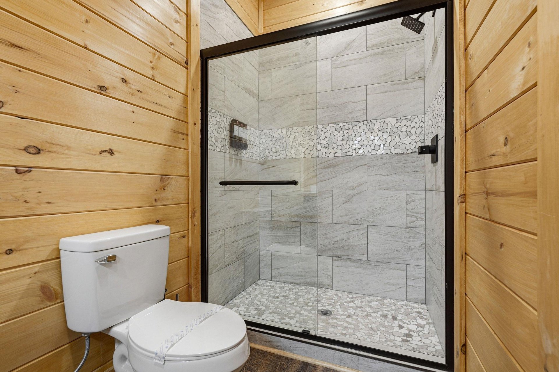 Step into your luxurious stonetiled shower with rainfall head and pebble flooring, perfectly complementing the warm wooden cabin walls.