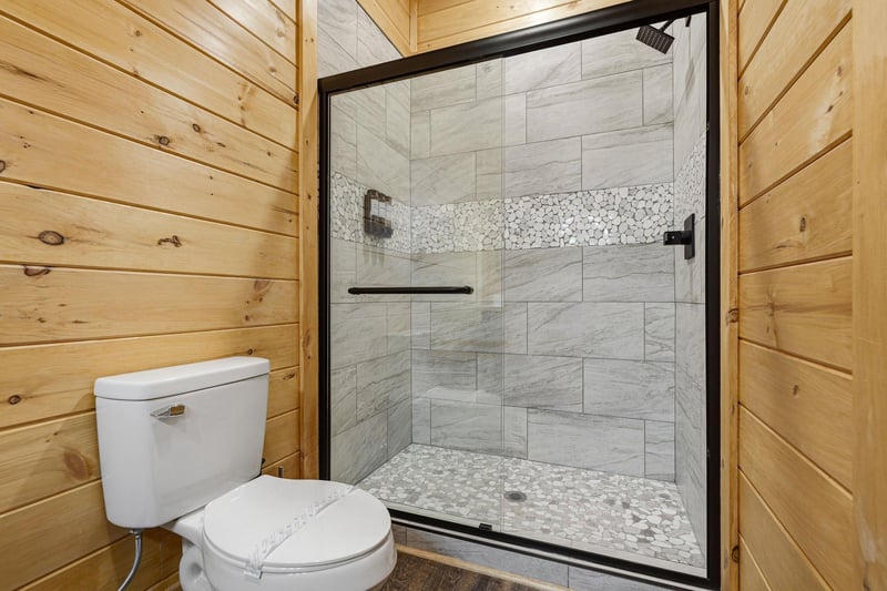 Step into your luxurious stonetiled shower with rainfall head and pebble flooring, perfectly complementing the warm wooden cabin walls.