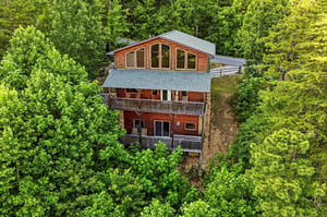A stunning threestory cabin nestled in a lush forest, featuring expansive windows, spacious balconies, and a unique architectural design perfect for a secluded mountain retreat.