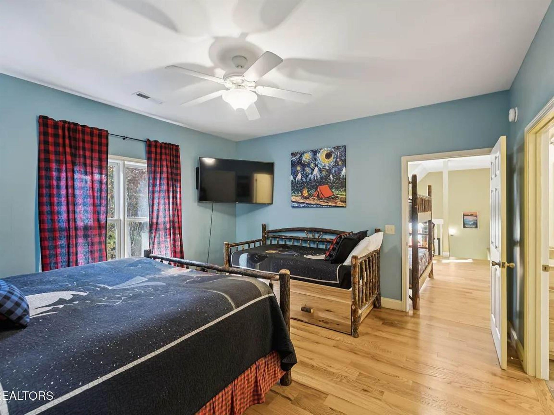 Spacious bedroom with a cozy bunk bed alongside a queen bed, perfect for families. Enjoy natural light from the window and stay comfortable with the ceiling fan overhead. Warm hardwood floors and char