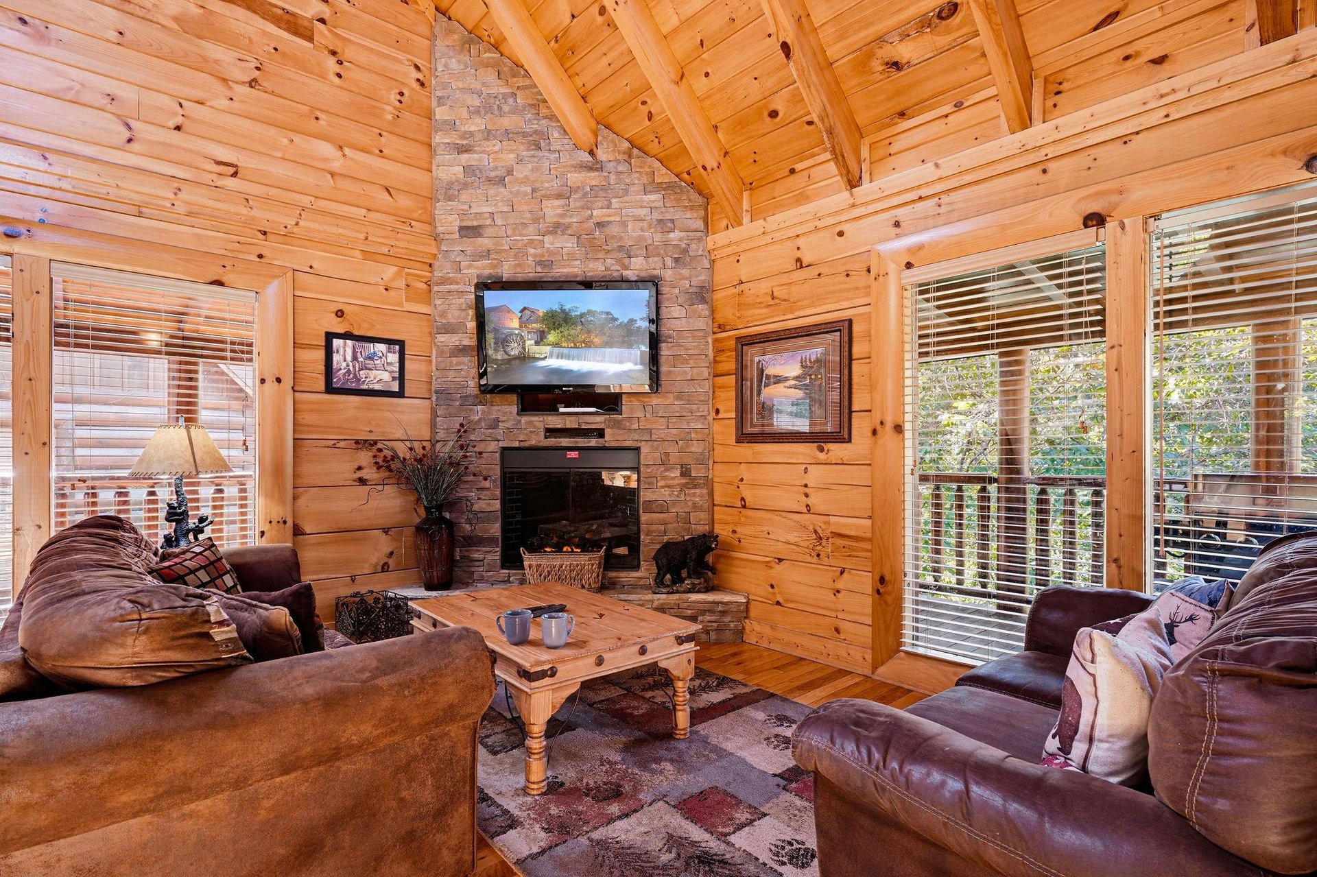Relax into plush leather seating beneath soaring timber beams and a stone fireplace. Your cabin retreat awaits with rustic warmth and natural light.
