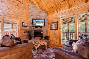 Relax into plush leather seating beneath soaring timber beams and a stone fireplace. Your cabin retreat awaits with rustic warmth and natural light.