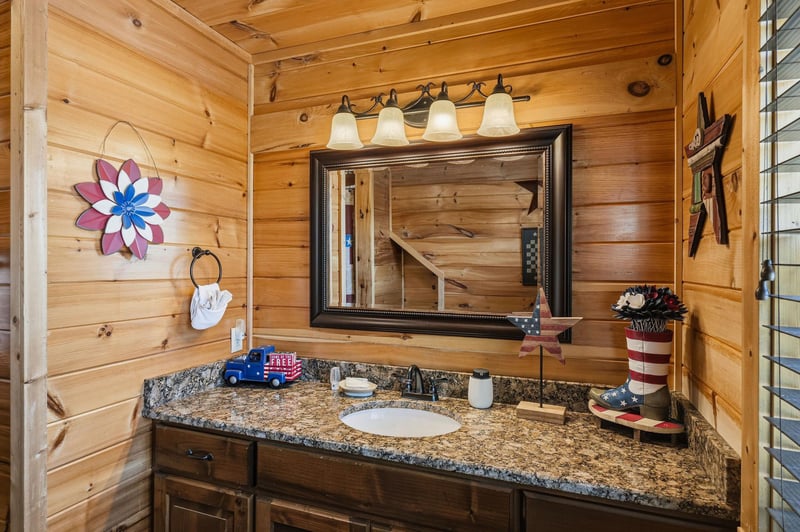 Warm wood paneling surrounds your granitetopped vanity, where soft lighting reflects in the framed mirror. Charming rustic touches make every morning feel cozy and welcoming.