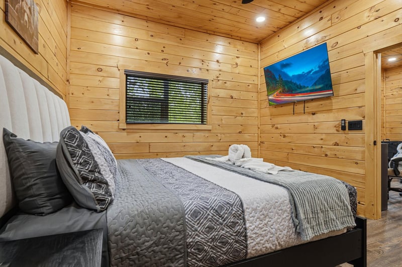Your cozy woodpaneled bedroom features a plush bed with soft linens, wallmounted TV, and charming towel animals awaiting your arrival.