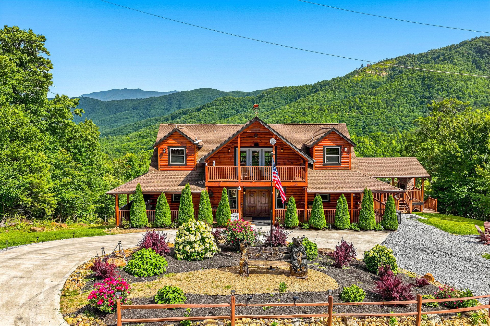 A stunning log cabin rental nestled in the lush mountain landscape, featuring colorful garden beds and dramatic views of surrounding forestcovered peaks.