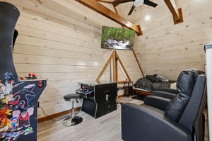 Unwind in your private game room featuring arcade games and cozy seating under rustic wooden beams.