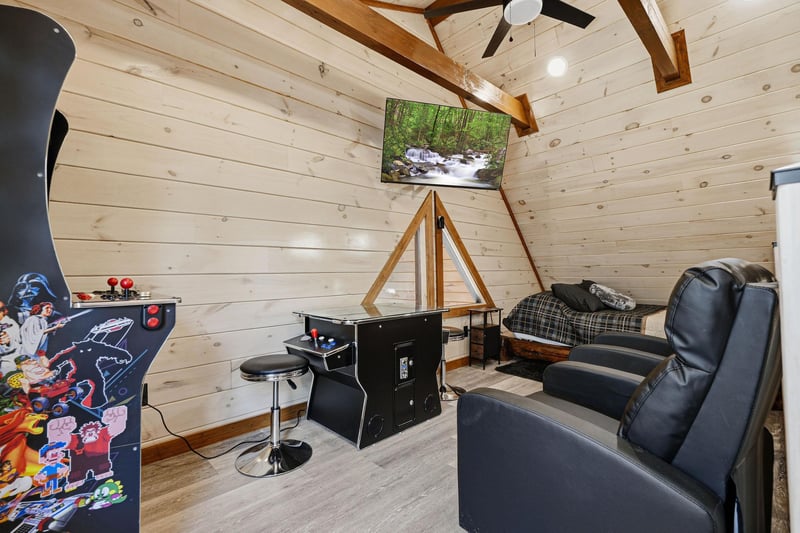 Unwind in your private game room featuring arcade games and cozy seating under rustic wooden beams.