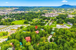 An aerial view captures the property nestled among lush greenery, with rolling mountains framing the vibrant community beyond.