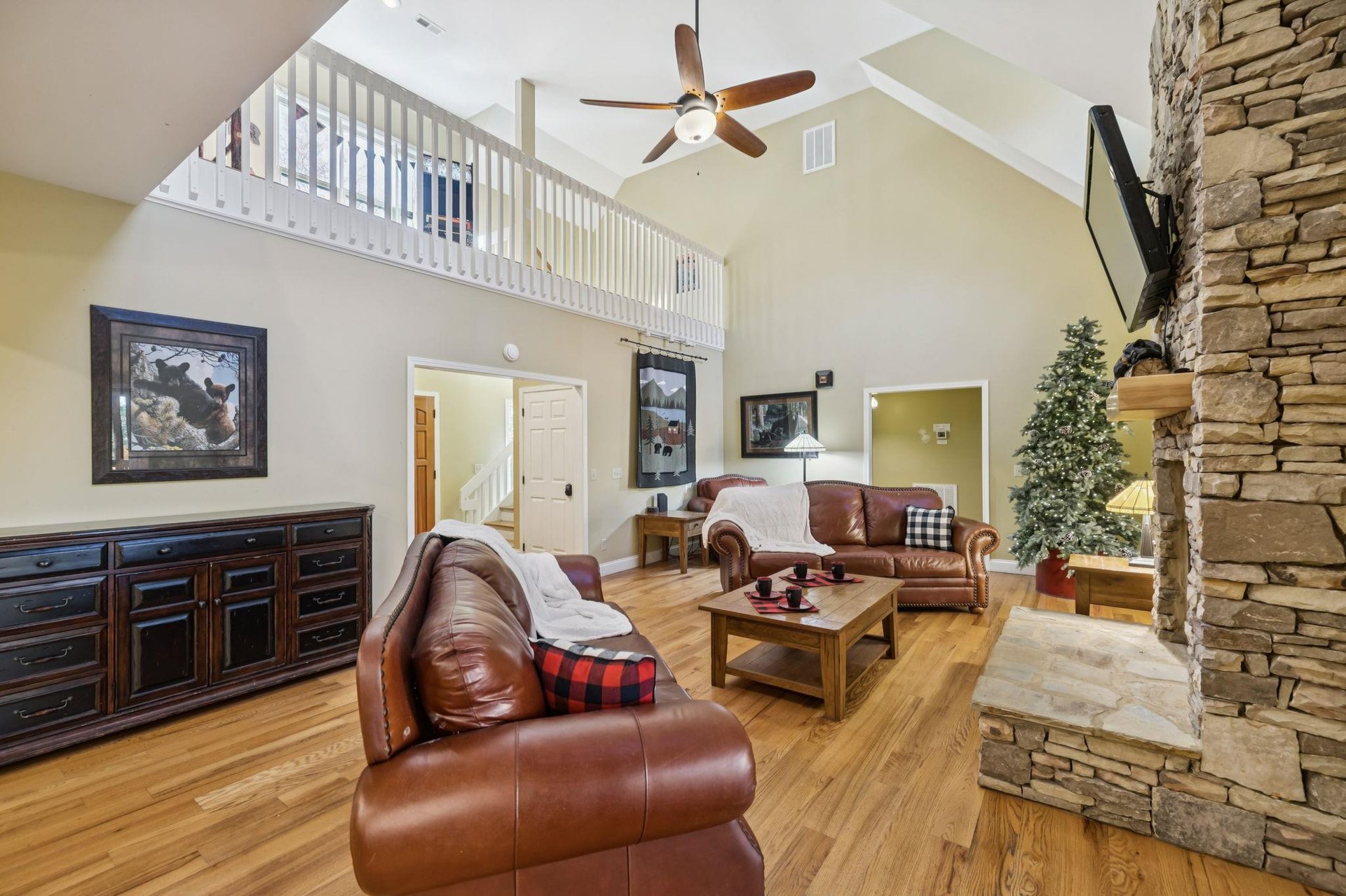 Your inviting living room features soaring cathedral ceilings, rich leather seating, warm wood floors, and a stunning stone fireplace—perfect for cozy evenings after exploring nearby attractions.