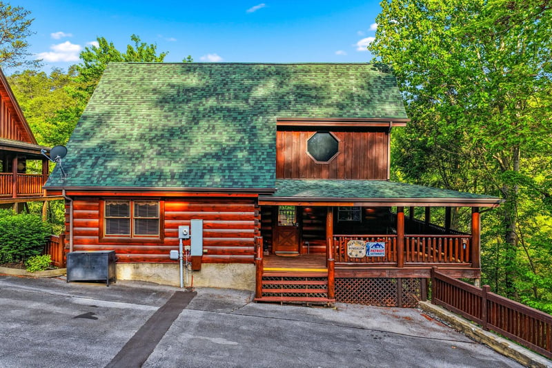 Charming log cabin featuring a wraparound deck and mountain setting surrounded by lush forest.