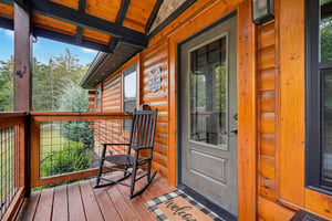 Welcome to your cozy cabin retreat, where a classic rocking chair awaits on your private covered porch, perfect for soaking in peaceful wooded views and fresh mountain air.