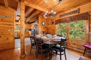 Gather around this handsome wooden table beneath a rustic chandelier as natural light pours in through tall windows. The cozy, cabinstyle warmth invites meals shared and memories made.