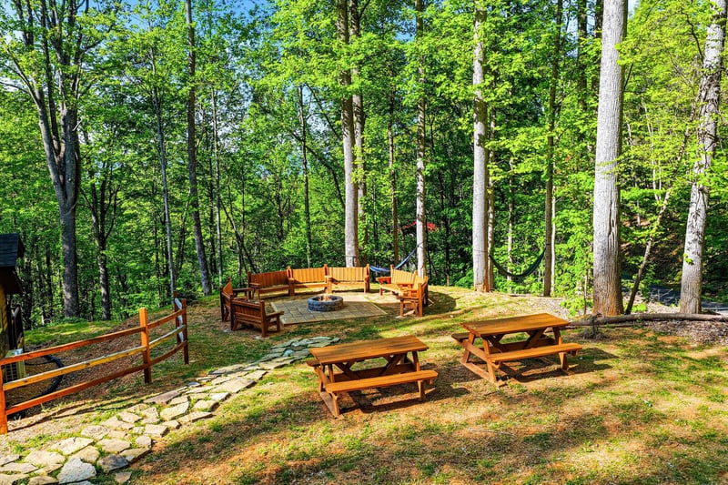 Gather around the fire pit for smores under towering trees, with picnic tables perfect for outdoor dining in this peaceful forest setting.