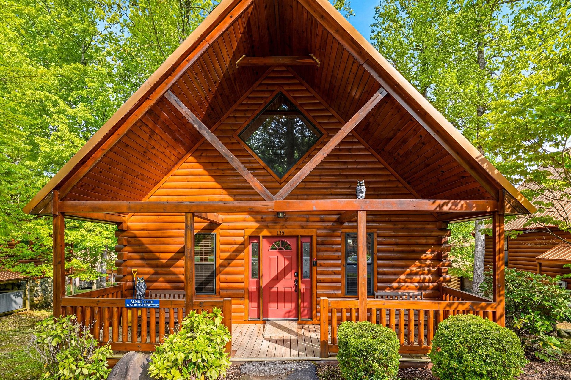 A stunning log cabin nestled among towering trees, featuring a welcoming red door and covered porch perfect for morning coffee.