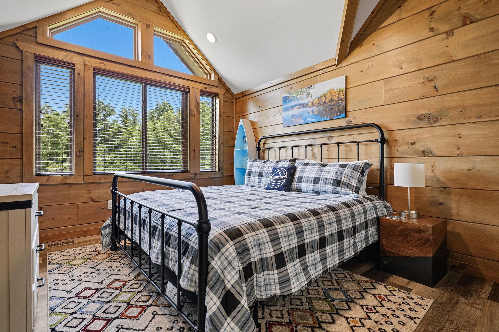 Wake up in this cozy woodpaneled bedroom where natural light streams through the large windows, offering peaceful forest views.