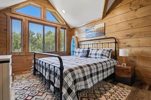 Wake up in this cozy woodpaneled bedroom where natural light streams through the large windows, offering peaceful forest views.