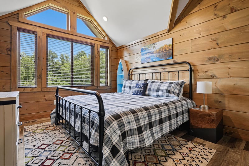 Wake up in this cozy woodpaneled bedroom where natural light streams through the large windows, offering peaceful forest views.