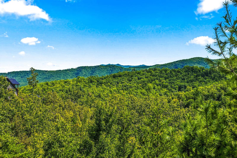 Nestled within a lush mountain landscape, the property offers an authentic immersion in nature. Rolling forested hills stretch toward blue mountain ridges beneath open skies.